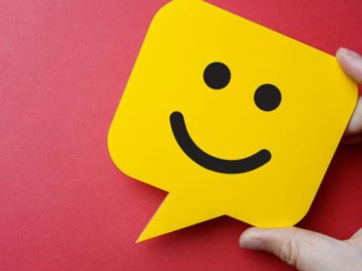 Customer service experience and business satisfaction survey. Man holding yellow speech bubble with smiley face on red background.