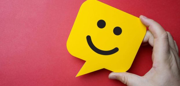 Customer service experience and business satisfaction survey. Man holding yellow speech bubble with smiley face on red background. Customer service experience and business satisfaction survey. Man holding yellow speech bubble with smiley face on red background.