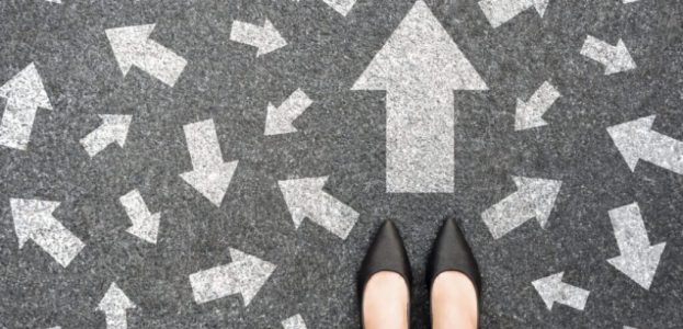 Feet and arrows on road background from above. Businesswoman standing on pathway with drawn white many direction arrows choice. Top view of A businesswoman black shoes. Motivation and growth concept. Feet and arrows on road background from above. Businesswoman standing on pathway with drawn white many direction arrows choice. Top view of A businesswoman black shoes. Motivation and growth concept.