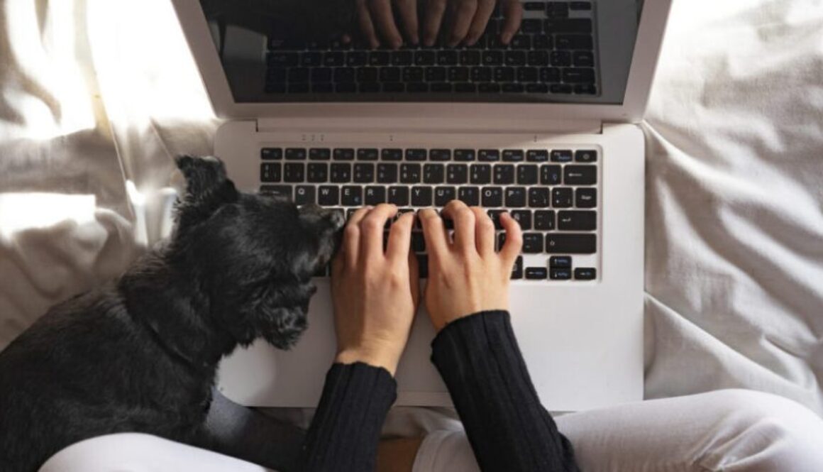 Top view of woman working with laptop at home next to her dog.