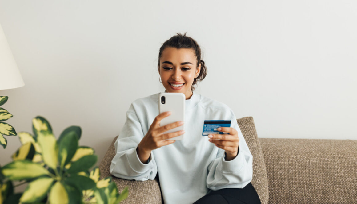 Smiling woman using smartphone and credit card. Young female making a purchase online.