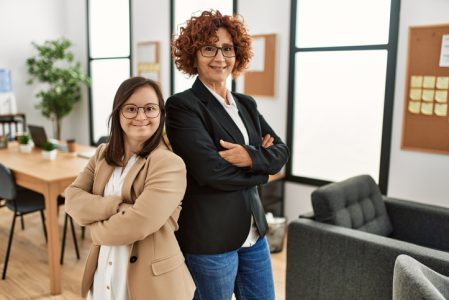 Group of two women working at the office. Mature woman and down syndrome girl working at inclusive teamwork. Group of two women working at the office. Mature woman and down syndrome girl working at inclusive teamwork.