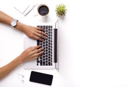 Woman typing on laptop on clean white office table with plant Woman typing on laptop on clean white office table with plant