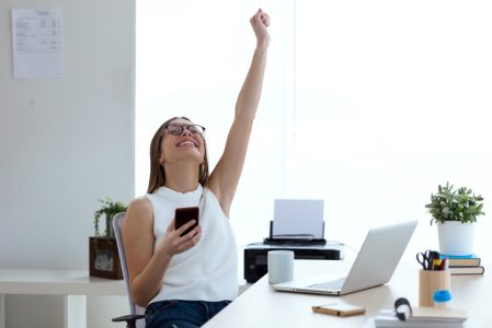 Business young woman celebrating a victory while working with mobile phone in the office. sindrome del impostor ib group
