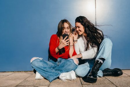 Couple of friends with long hair, one blonde and the other brunette, listening to music from their cell phones. crea contactos
