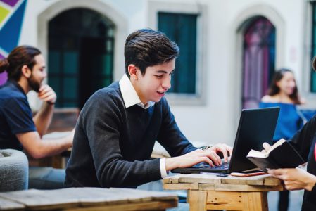 Young latin college man sitting while using computer at university in Mexico Young latin college man sitting while using computer at university in Mexico
