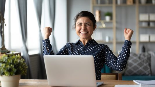 Euphoric young indian girl celebrate online victory triumph with laptop Euphoric young indian girl celebrate online victory triumph with laptop
