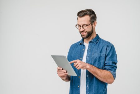 Cheerful caucasian young man student freelancer using digital tablet for social media, e-banking, mobile application, e-learning isolated in white background Cheerful caucasian young man student freelancer using digital tablet for social media, e-banking, mobile application, e-learning isolated in white background