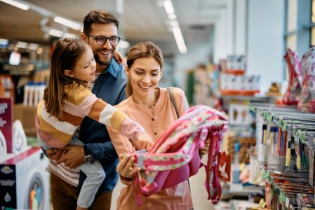 Happy little girl pointing at backpack while buying school supplies with her parents in supermarket. Happy little girl pointing at backpack while buying school supplies with her parents in supermarket.