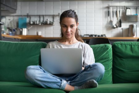 Serious woman using laptop checking news online sitting on sofa Serious woman using laptop checking news online sitting on sofa